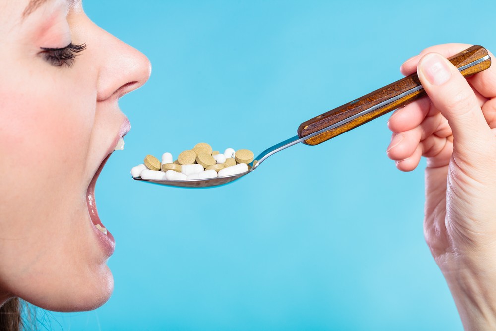 Concept of health care or abuse and addiction tablets. Young woman eating pills on a spoon on blue